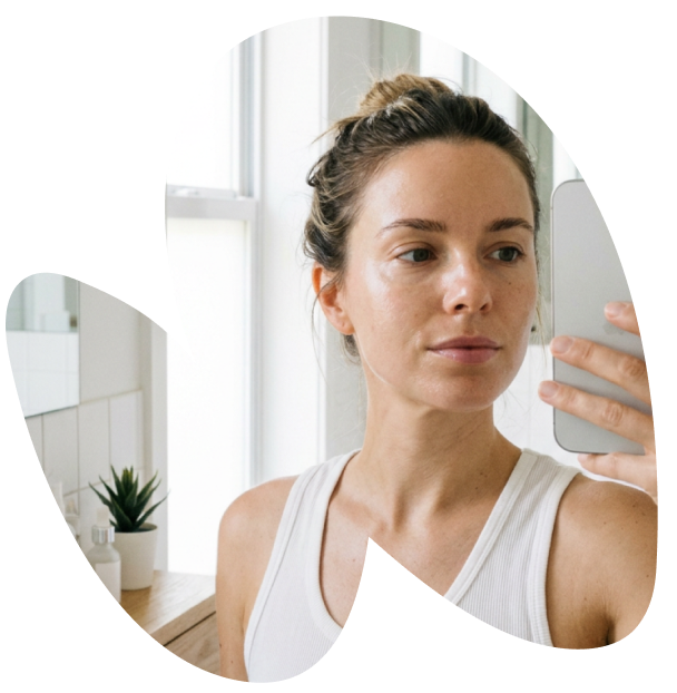 Woman taking mirror selfie in bathroom with skincare products